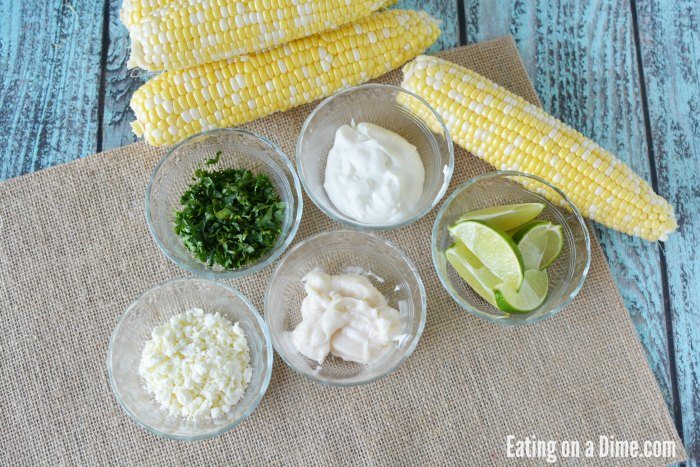Close up image of ingredients needed to make Mexican Corn on the cob - Corn on the cob, sour cream, mayonnaise, minced garlic, chili powder, chopped cilantro feta cheese