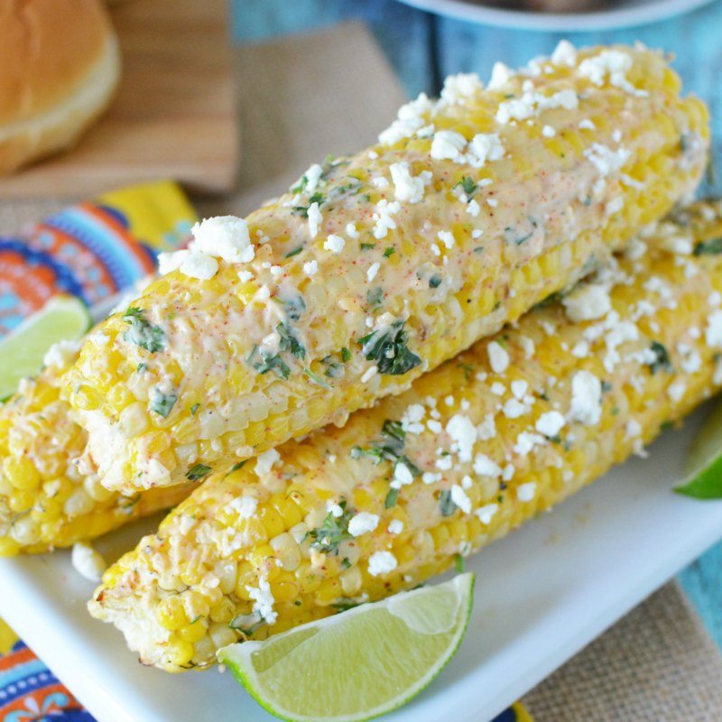Close up image of Mexican Corn on the Cob on a white plate with lime wedges.
