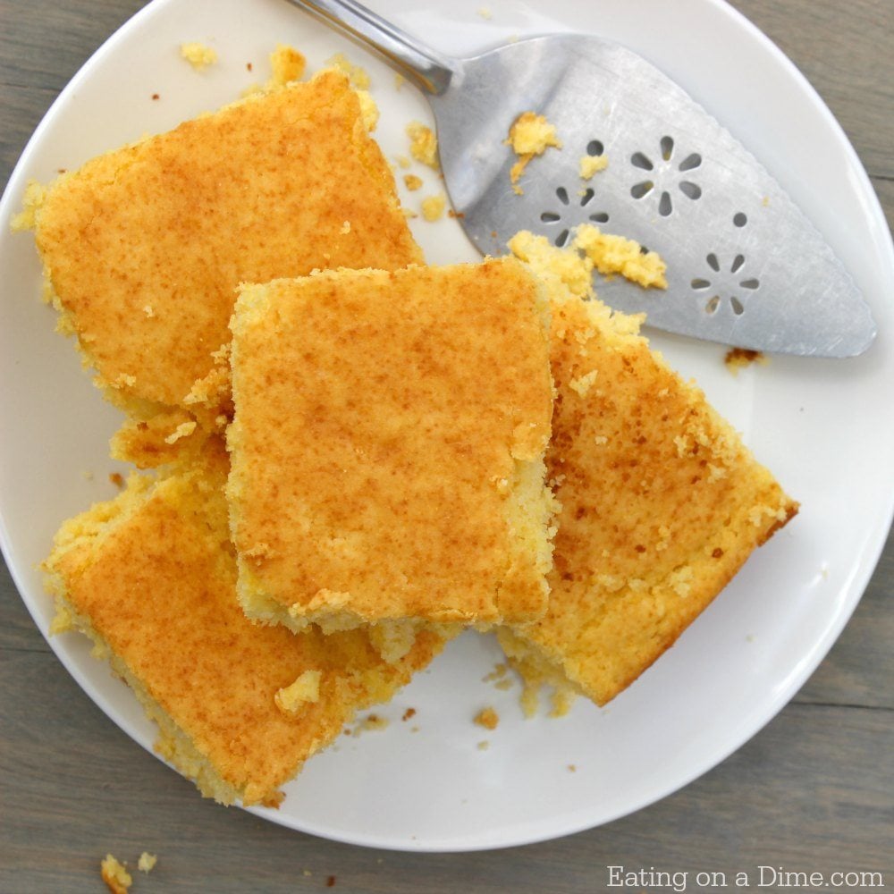 Close up image of cornbread serving size on a white platter with a serving utensil. 