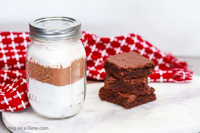 Close up image of brownies stack and a mason jar of brownie mix with a red hand towel. 