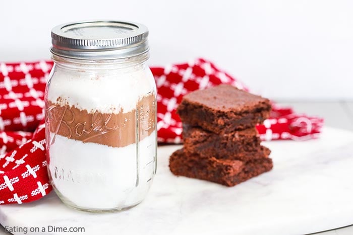 Close up image of mason jar of brownie mix with a stack of brownies. 