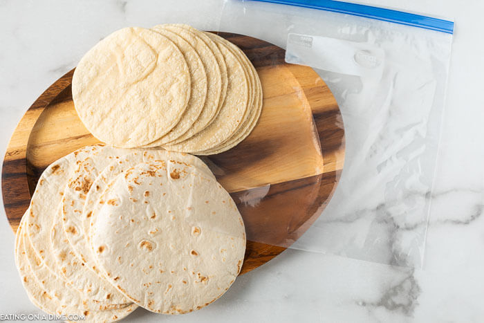 Flour and Corn tortillas on a wooden platter with a freezer bag next to it. 