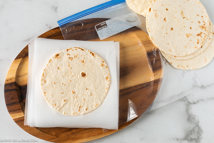 Flour Tortillas on a wooden platter with parchment paper in between each tortillas 