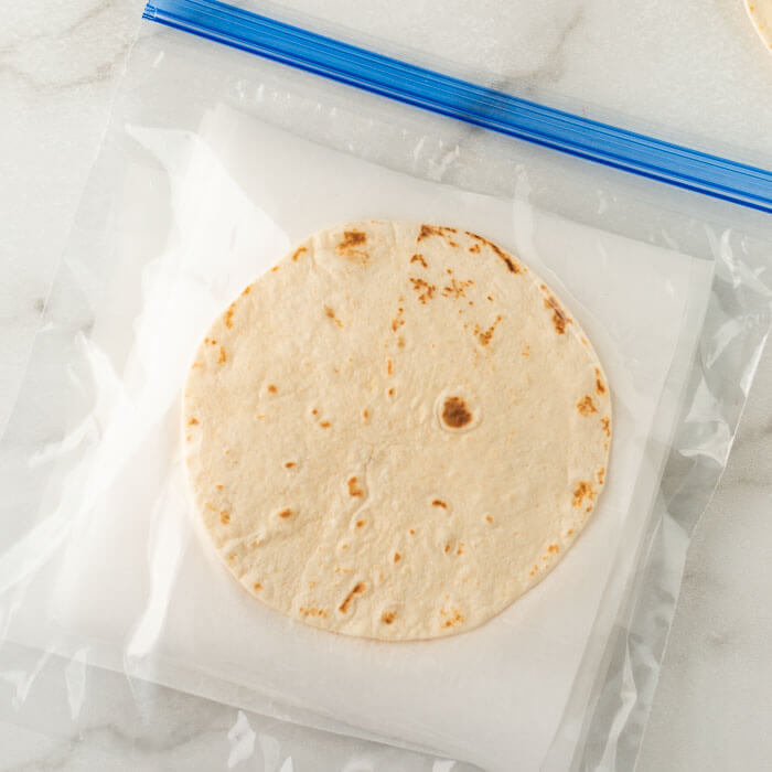 Flour tortillas in a freezer bag with parchment paper in between each tortillas. 