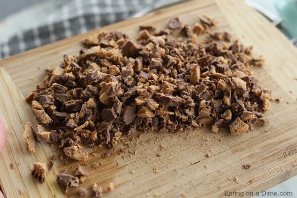 This Peanut Butter Reese’s Pie Recipe is the perfect no bake dessert. Reese's peanut butter pie recipe is delicious. Try Reese's chocolate peanut butter cup pie for an easy dessert recipe. This is the best Peanut Butter Pie easy no bake recipe. The entire family will love Reese’s Chocolate Peanut Butter Pie Recipe! #eatingonadime #pierecipes #dessertrecipes #reesesrecipes #easydesserts Close up image of a Reese's peanut butter cups being chopped on a cutting board.
