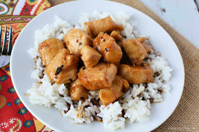 Close up image of a white plate of teriyaki chicken on a bed of rice. 