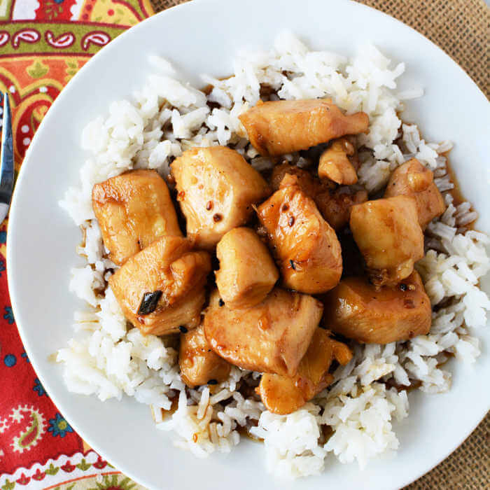 Close up image of a white plate of teriyaki chicken on a bed of rice. 