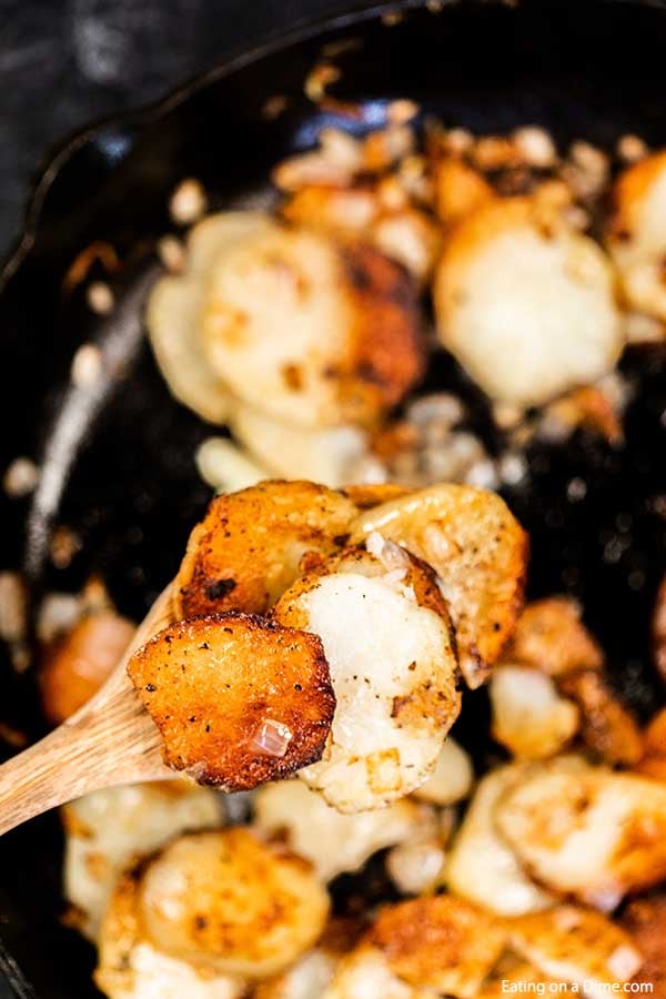 Pan fried potatoes in a skillet with a wooden spoon