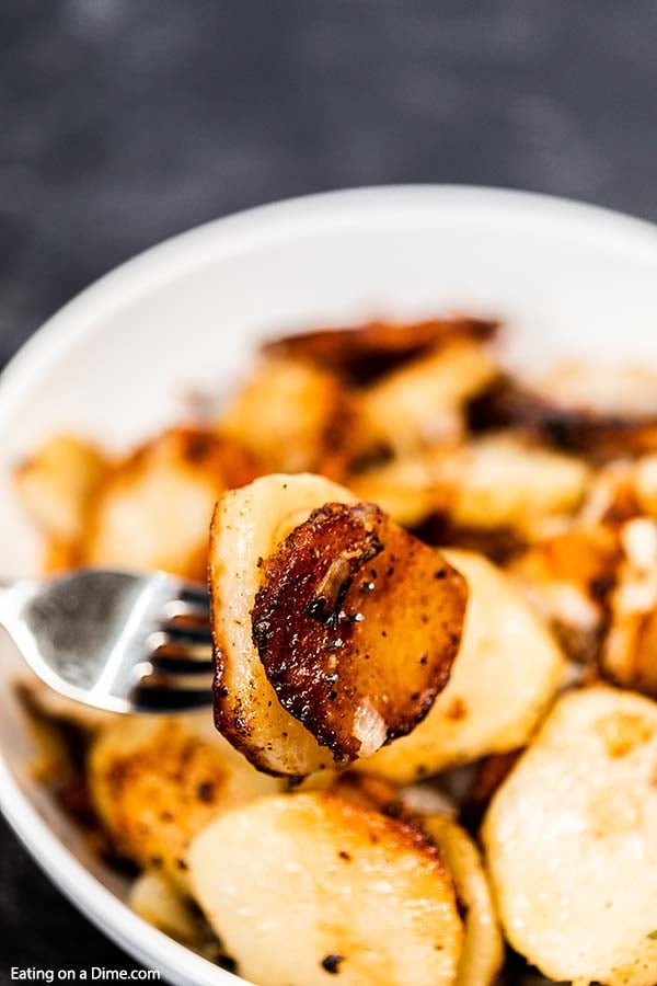 Pan fried potatoes in a bowl with a bite on the fork