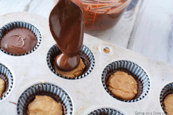 Close up image of homemade peanut cups in process with chocolate being spooned over the peanut butter. 