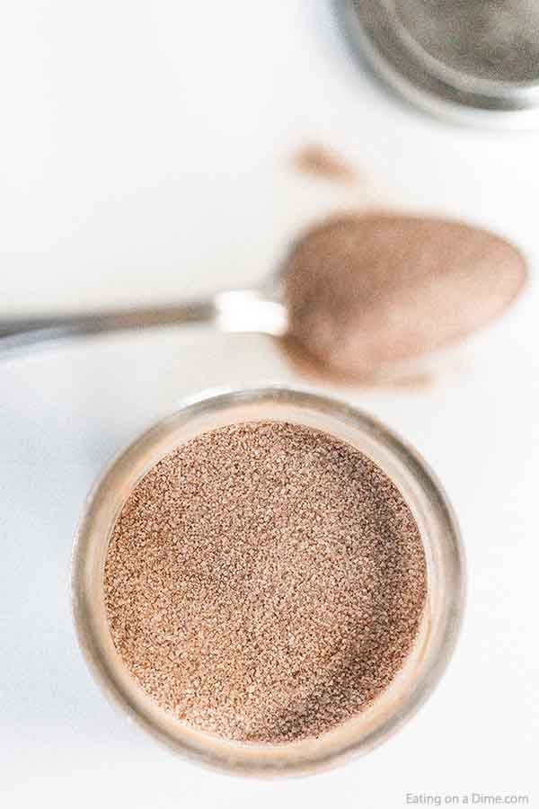 A jar of cinnamon sugar mixture with a spoon full of the mixture next to it. 