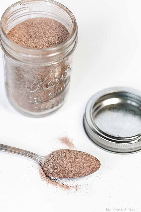 A jar of cinnamon sugar mixture with a spoon full of the mixture next to it. 