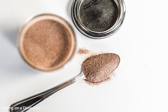 A jar of cinnamon sugar mixture with a spoon full of the mixture next to it. 