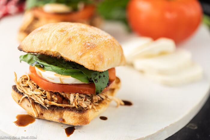 Closeup photo of balsamic pulled chicken sliders on a bun with tomato, mozzarella and fresh basil. 