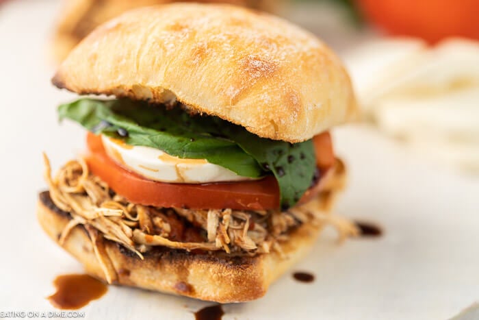 Closeup photo of balsamic pulled chicken sliders on a bun with tomato, mozzarella and fresh basil. 