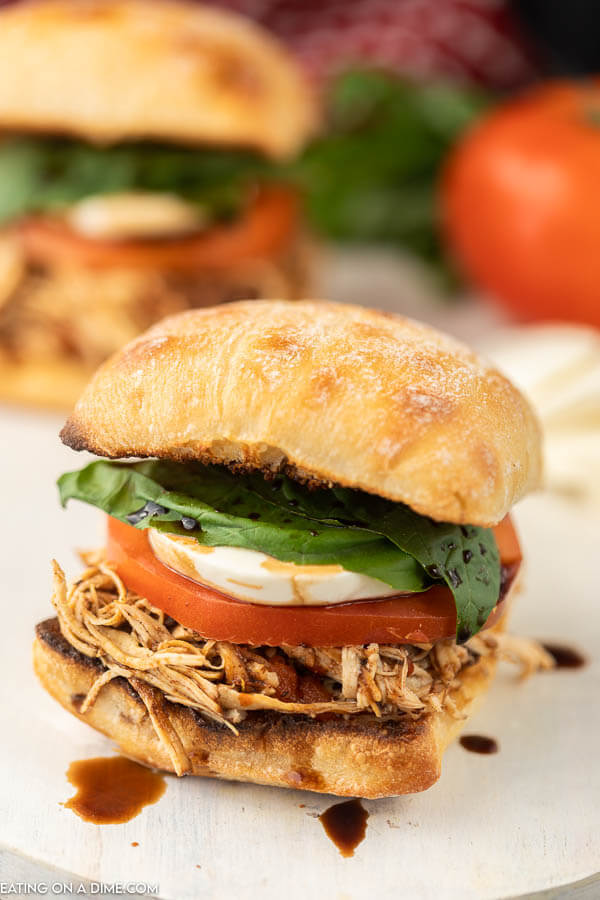 Closeup photo of balsamic pulled chicken sliders on a bun with tomato, mozzarella and fresh basil. 