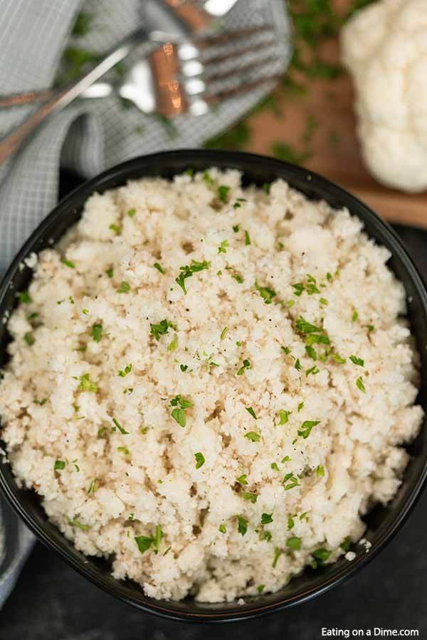 A black bowl of cauliflower rice seasoned with cilatro. 