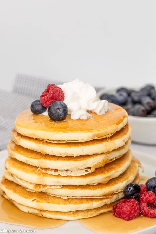 Prepared pancakes stacked on top of each other topped with whipped cream and fresh berries. 