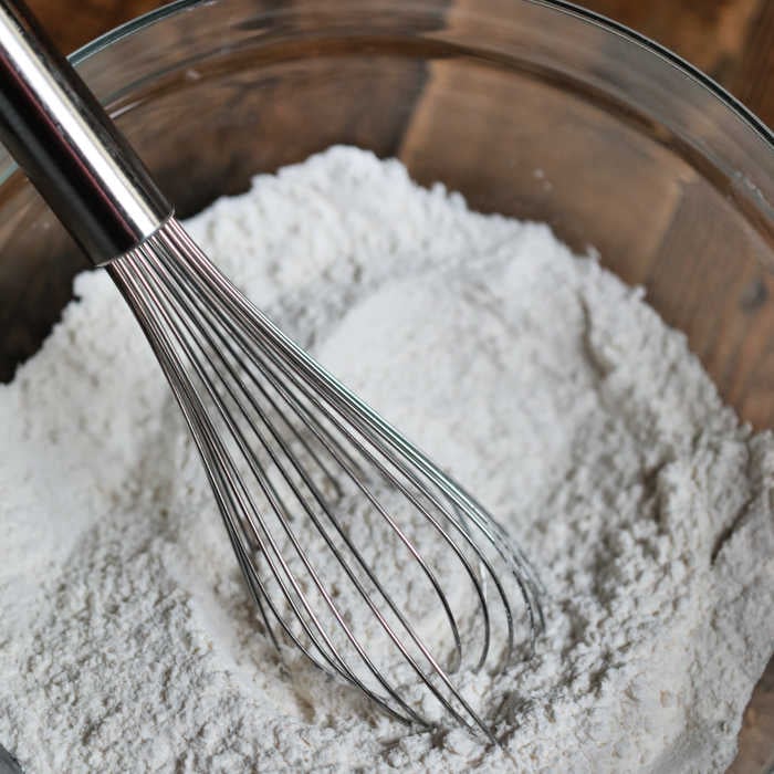 Close up image of prepared pancake mix in a clear bow with a whisk. 