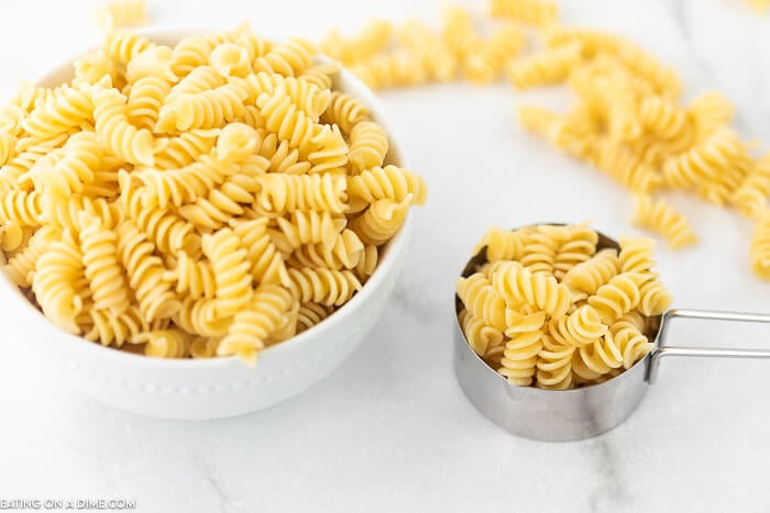 Cooked rotini pasta in a bowl and a measuring cup on a counter.  