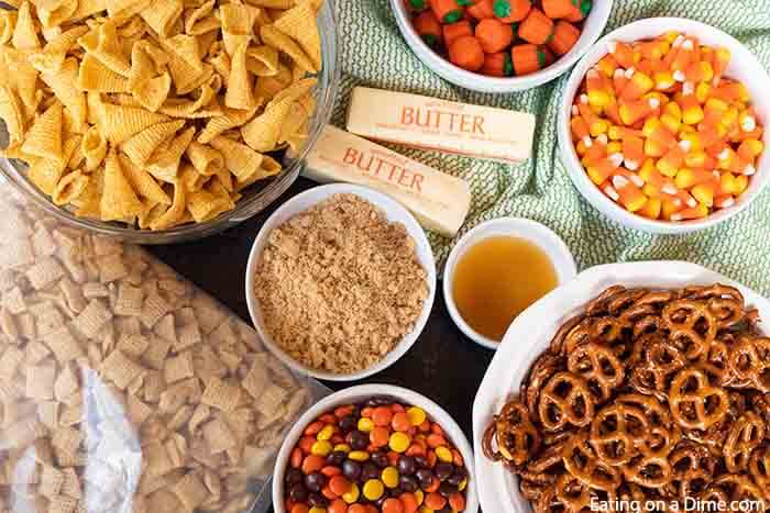 Ingredients Halloween Snack Mix - Bowls of bugels, pumpkin candy, candy corn, sticks of butter, bowl of brown sugar, pretzels and Reese's Pieces