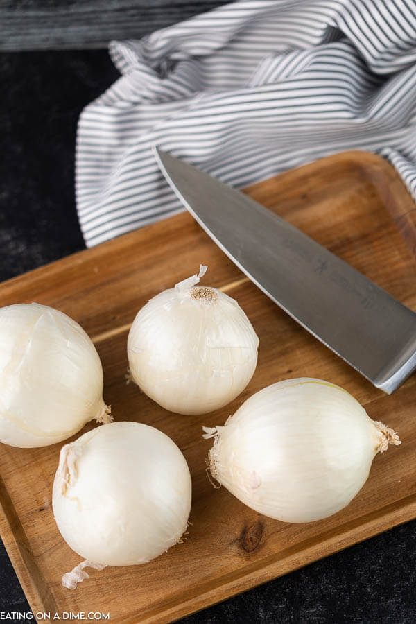 Onions on a cutting board with a knife next to it.  