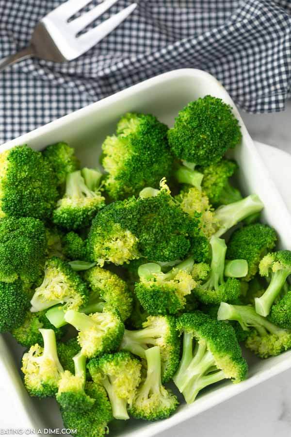 Steamed broccoli in a microwave safe dish with a large fork behind it. 