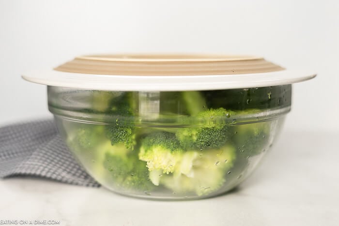 Fresh broccoli in a glass bowl with a plate on top 