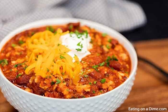 Close up image of turkey chili in a white bowl topped with cheese and sour cream. 