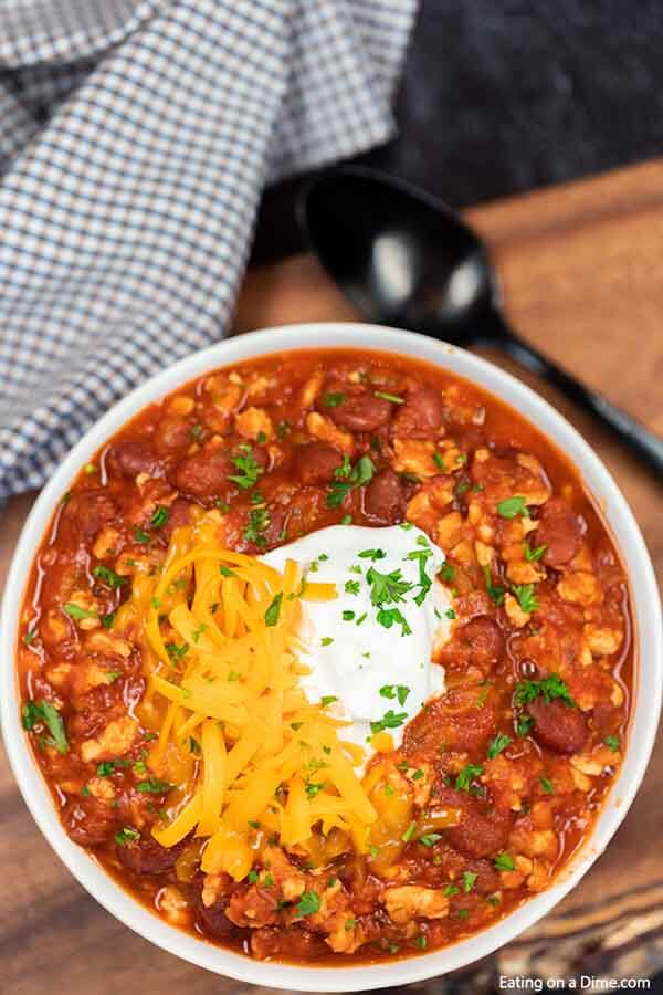 Close up image of turkey chili in a white bowl topped with sour cream and cheese. 