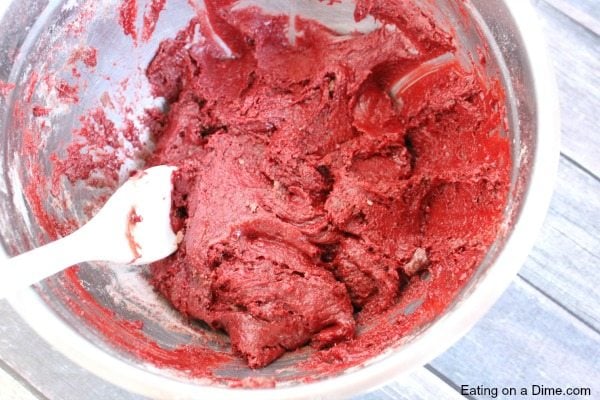 Close up image of a red velvet cookie being mixed in a glass bowl with a wooden spoon. 