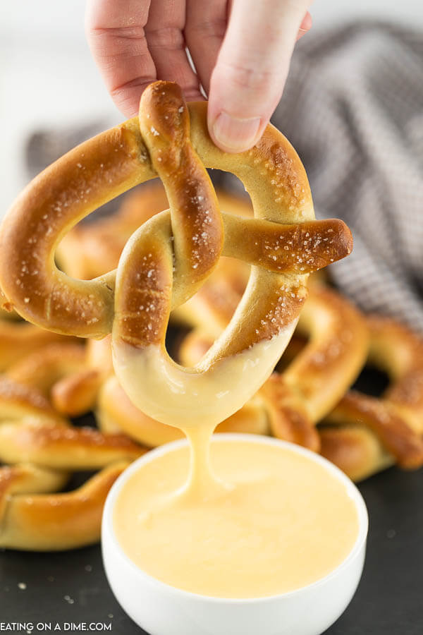large pretzel being dipped into cheese sauce