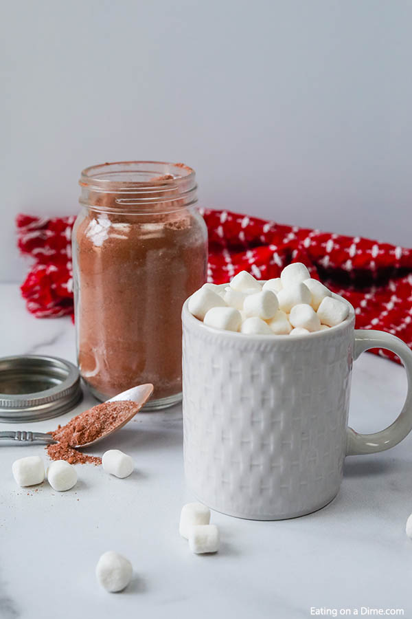 Close up image of hot chocolate mix with a white mug of hot chocolate with marshmallows. 