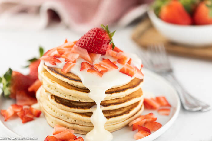 Closeup photo of a stack of strawberry pancakes with cream cheese glaze. 