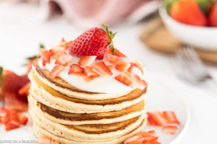 Closeup photo of a stack of strawberry pancakes with cream cheese glaze. 