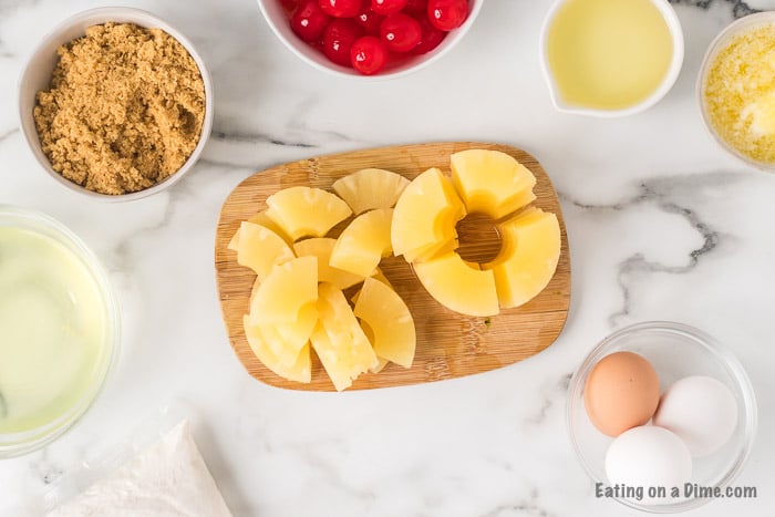 A photos of the ingredients needed to make the cupcakes: Pineapples, cake mix, vegetable oil, eggs, butter, brown sugar and cherries 