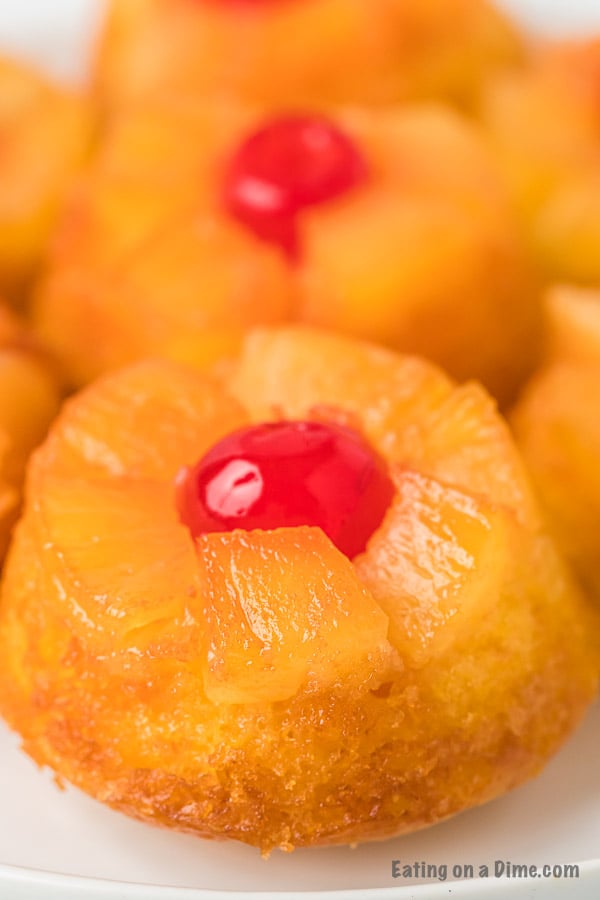 Close up of an Upside Down Pineapple Cupcake on a white plate with another cupcake behind it. 