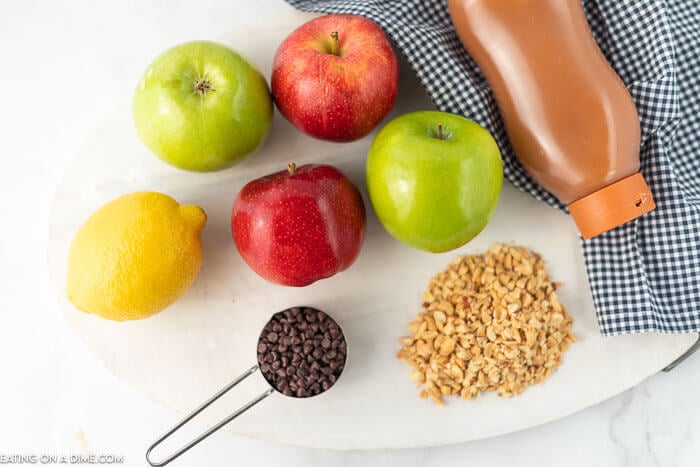 Apples, lemon, measuring cup with chocolate chips, chopped nuts and caramel sauce
