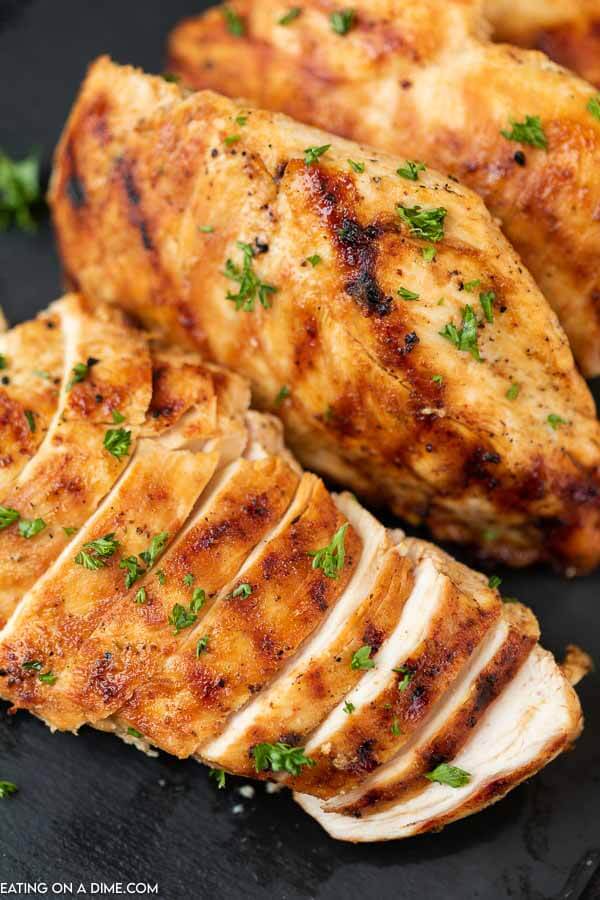Grilled Chicken on a black platter and 1 piece of the chicken is sliced 