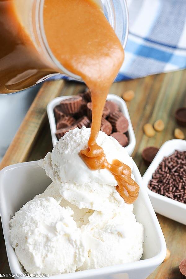The peanut butter topping is being poured onto ice cream in a white bowl. 