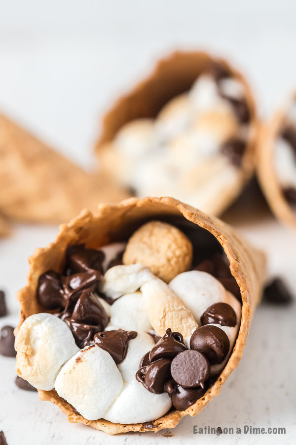 Check out how to make s’mores campfire cones that are fun and less messy than traditional s’mores. Camp fire cones are a blast and fun to make. Campfire sugar cone s’mores are a fun and easy dessert for any camping treat. Campfire s’mores cones will be your favorite summer treat! #eatingonadime #smoresrecipes #campfirecones #easydesserts 