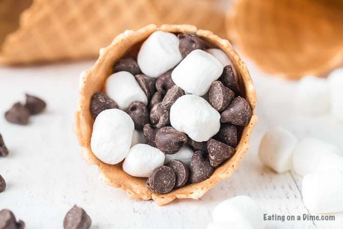 Check out how to make s’mores campfire cones that are fun and less messy than traditional s’mores. Camp fire cones are a blast and fun to make. Campfire sugar cone s’mores are a fun and easy dessert for any camping treat. Campfire s’mores cones will be your favorite summer treat! #eatingonadime #smoresrecipes #campfirecones #easydesserts 