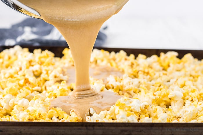 Pouring the melted caramel mixture over the popcorn on a baking sheet