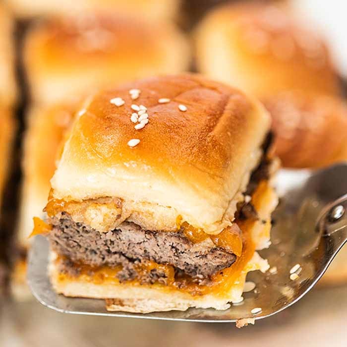 A close up of a cheeseburger slider being served on a spatula.  