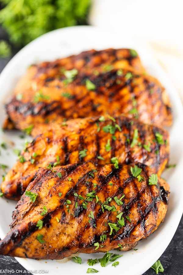 grilled chicken stacked on a white plate topped with fresh parsley 