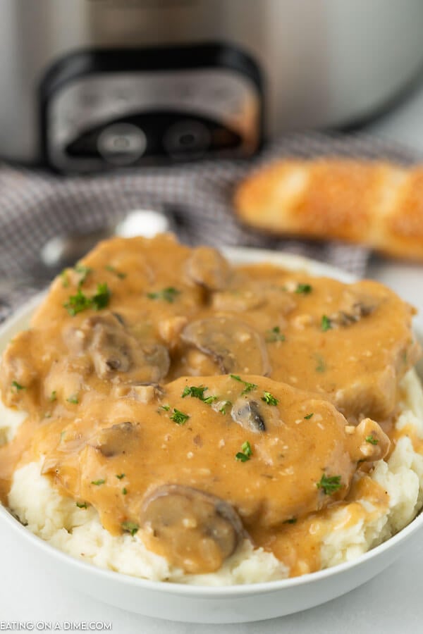 Close up image of smothered pork chops on mashed potatoes in a white bowl. 