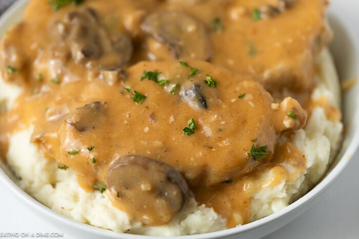 Close up image of smothered pork chops on mashed potatoes in a white bowl. 