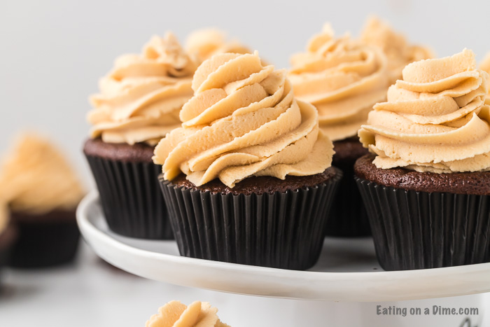 Close up image of several chocolate peanut butter cupcakes on a cake stand. 
