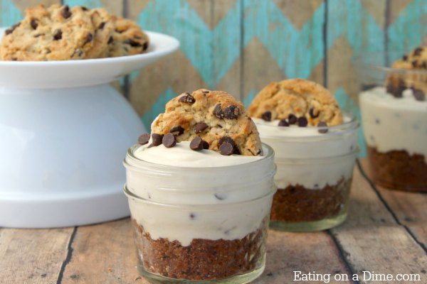 A jar with the no bake chocolate chip cookie cheesecake in it topped with a cookie with twine tied around the jar. 