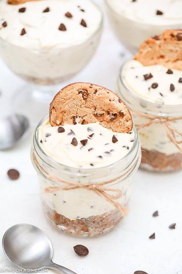 A jar with the no bake chocolate chip cookie cheesecake in it topped with a cookie. 